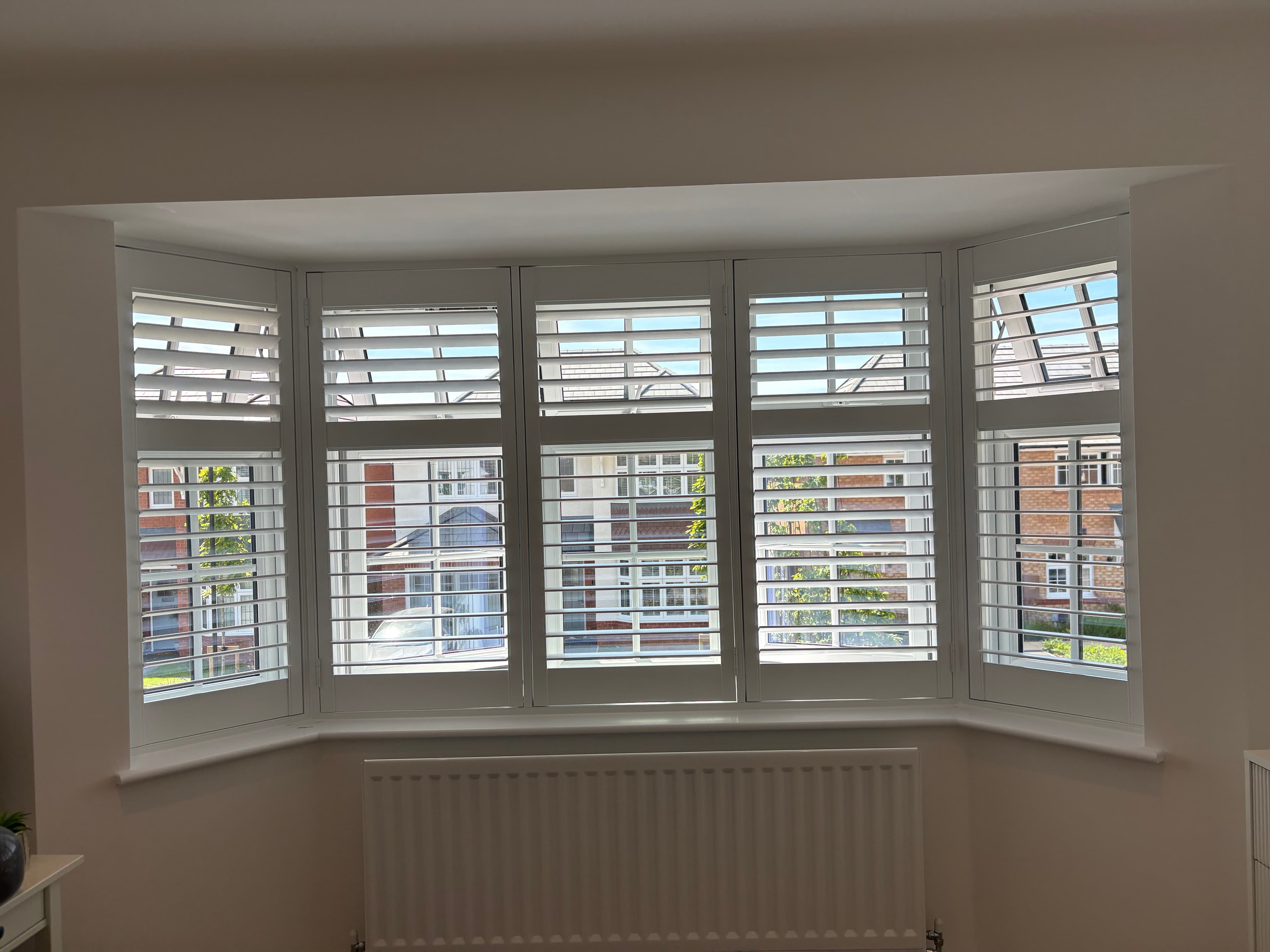 White tier-on-tier plantation shutters fitted to a five-panel bay window with a radiator below