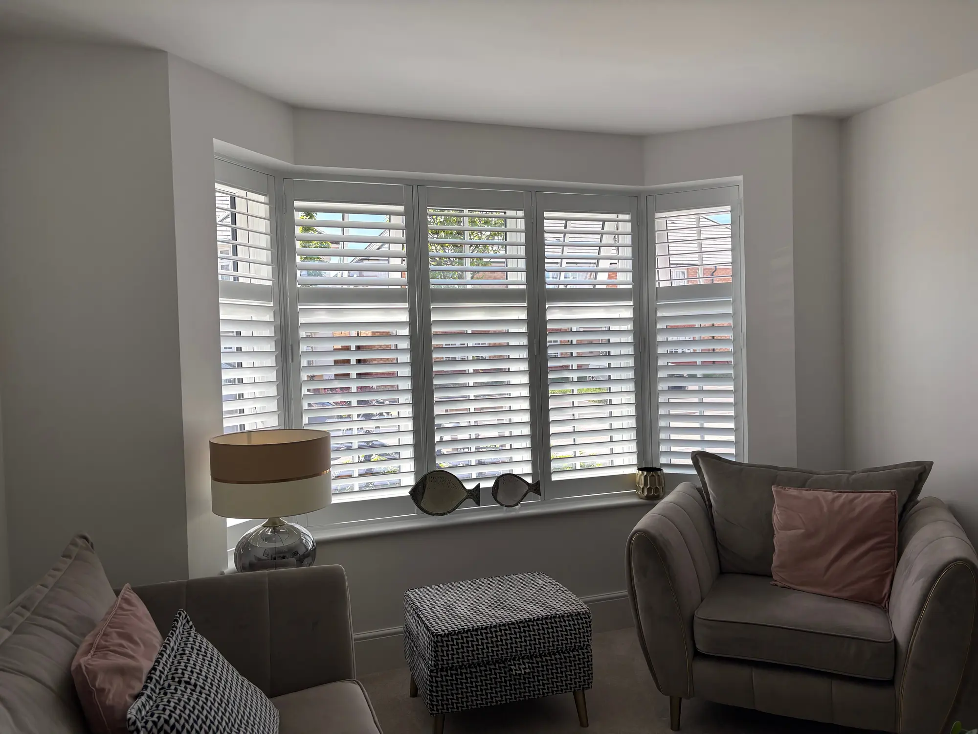 White tier-on-tier shutters fitted across a five-panel bay window in a living room