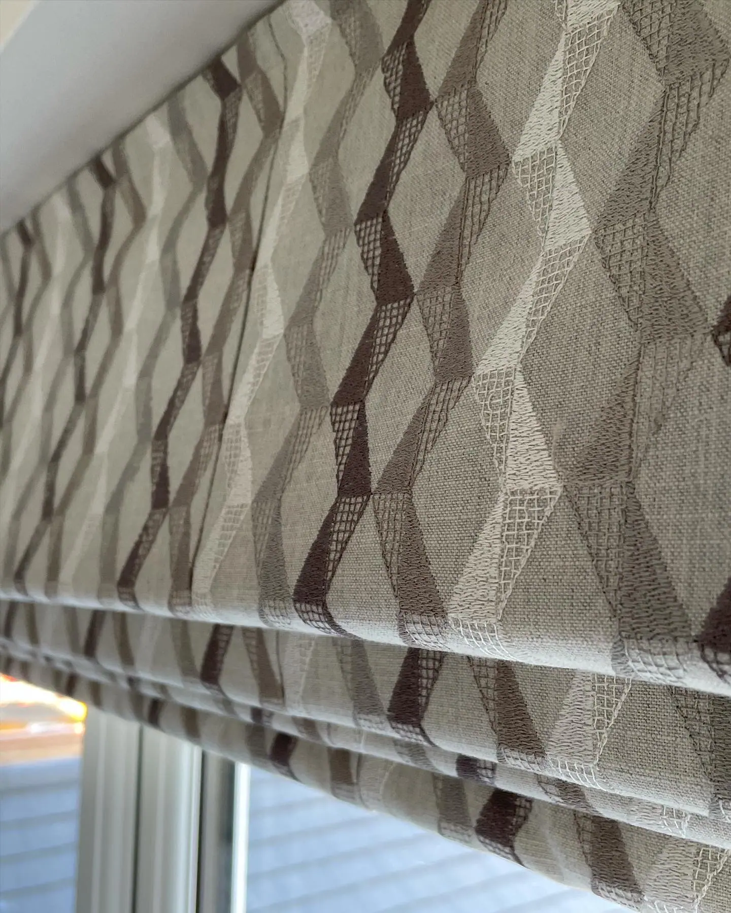 Close-up of a roman blind in a taupe and grey embroidered diamond pattern