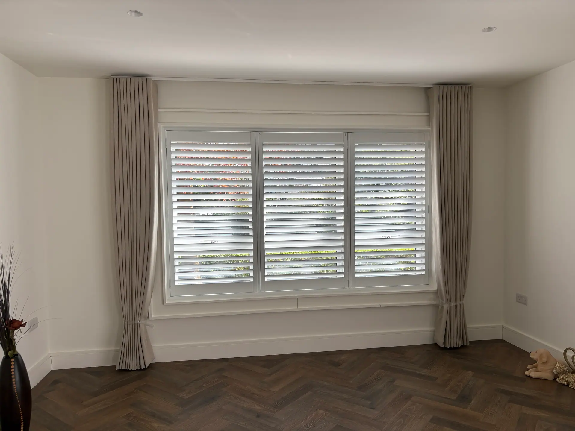 Made-to-measure linen curtains framing three-panel white shutters on a bedroom window