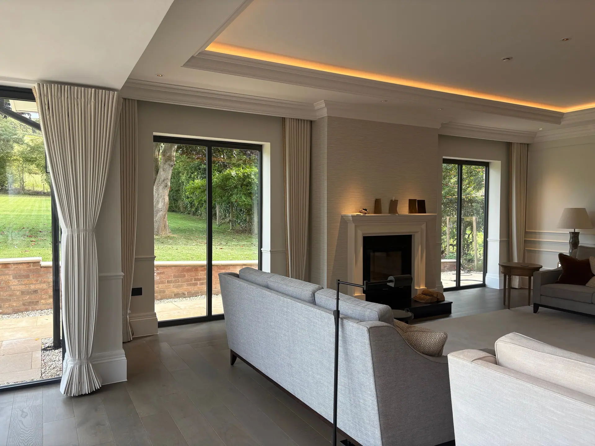 Cream pleated curtains beside garden doors in an elegant living room with a fireplace